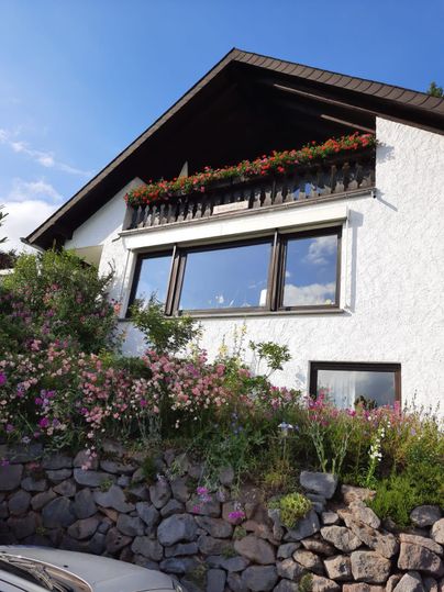 Ein charmantes Haus mit einem Balkon, der mit Blumen geschmückt ist. Der Garten ist bunt bepflanzt und der Himmel ist klar.