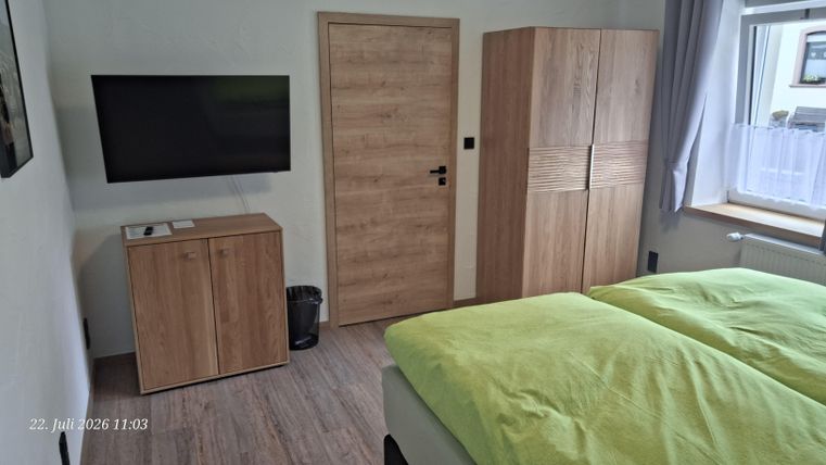 Ein modernes Schlafzimmer mit einem Doppelbett und hellgrünen Decken. An der Wand befindet sich ein Fernseher sowie ein Holzschrank und eine Kommode.