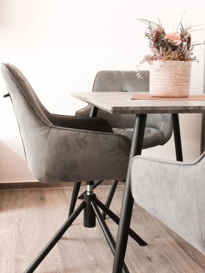 Ein moderner Essbereich mit grauen Stühlen und einem Tisch aus Holz. Auf dem Tisch steht ein Blumenarrangement in einem Blumentopf.