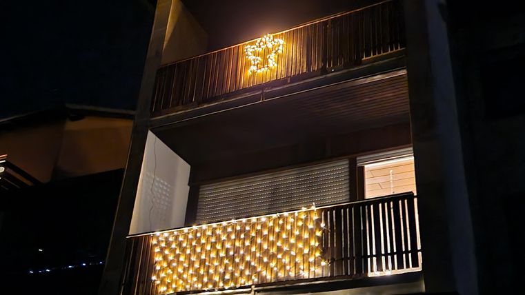 Een modern gebouw met twee balkons, die feestelijk zijn versierd met lichten. Het is nacht, en de lichten stralen fel tegen de donkere achtergrond.