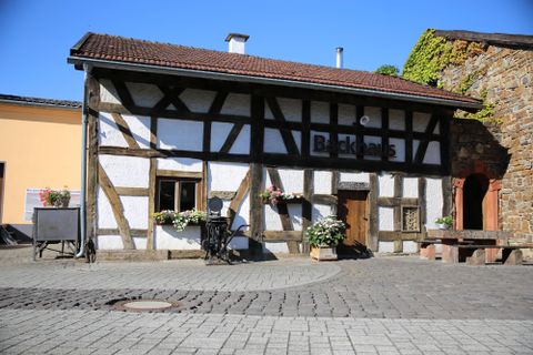 Ein kleines Fachwerkhaus auf einem großen Hof. Über der Eingangstür steht der Schriftzug "Backhaus".