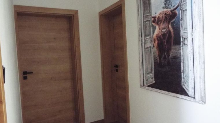 Ein heller Flur mit zwei Holztüren und einem großen Bild eines Highlandrinds an der Wand. Die Türen sind aus Holz und die Wände sind in sanften Farben gehalten.