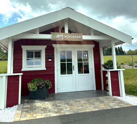 Ein rotes Holzhaus mit einem weißen Dach und einer einladenden Eingangstür. Vor dem Haus stehen Pflanzen in Töpfen und der Bereich ist gepflegt.