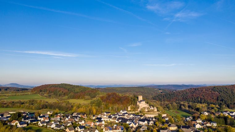 Luftaufnahme von Kerpen mit einer Burg im Zentrum, umgeben von Häusern und grüner Landschaft unter klarem, blauem Himmel.
