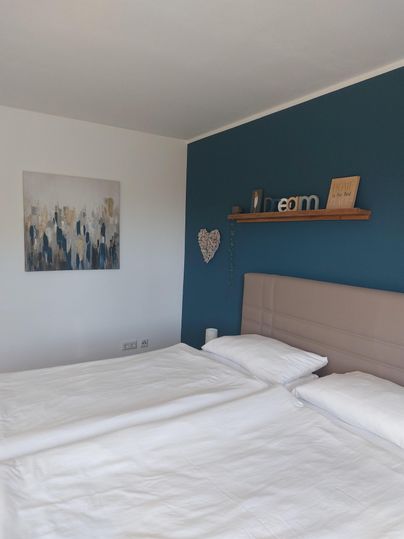 Une chambre moderne avec un lit double et des draps blancs frais. Sur le mur, il y a une image et une étagère avec des éléments décoratifs.