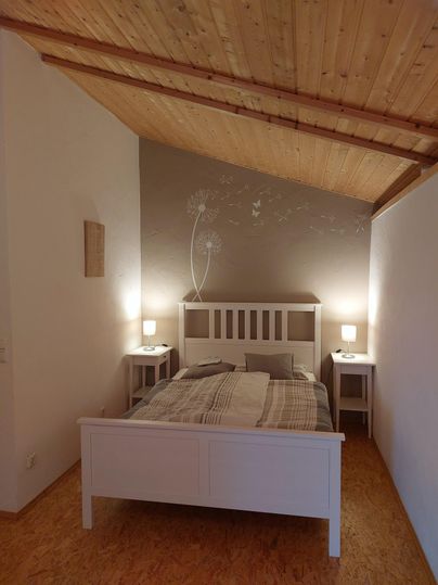 Une chambre lumineuse avec un lit blanc et un plafond en bois. À côté du lit, il y a deux tables de nuit avec des lampes.