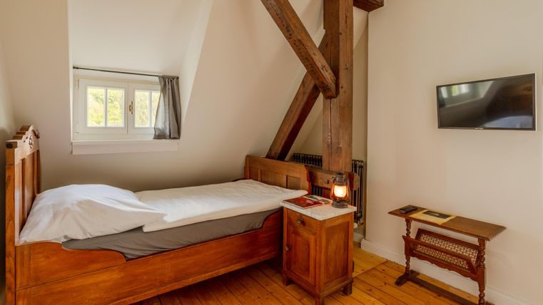 Ein gemütliches Schlafzimmer mit einem Einzelbett und Holzbalken. An der Wand befindet sich ein Fernseher und ein Tisch aus Holz.
