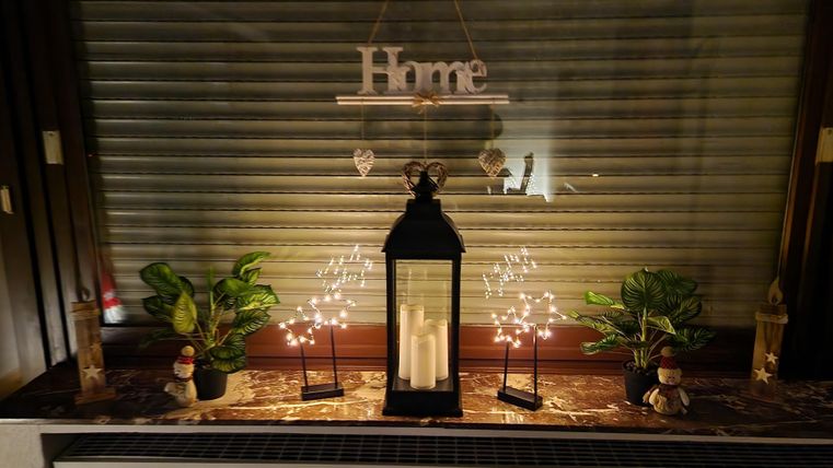 Een gezellige vensterbank met een lantaarn, lichtjes en planten. De tekst "Home" zorgt voor een uitnodigende sfeer.