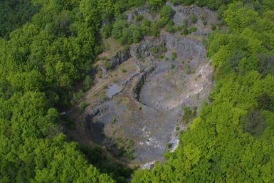 Vue aérienne d'un cratère boisé avec des roches nues et des chemins.