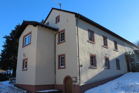 Ein großes, beige-rot gestrichenes Haus im Schnee. Der Himmel ist klar und blau, was auf einen sonnigen Tag hindeutet.