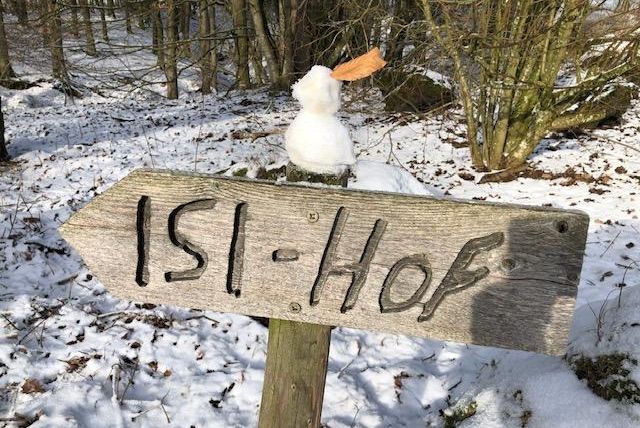 Een besneeuwd bord naar een plek genaamd "Isi-Hof". Boven op het bord zit een klein sneeuwmannetje.