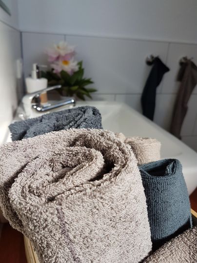 Ein schöner Badezimmerbereich mit gestapelten, sauberen Handtüchern in verschiedenen Farben. Im Hintergrund sind ein Waschbecken und eine Pflanze sichtbar.