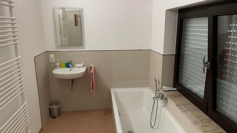 Une salle de bain moderne avec une baignoire et un lavabo. Les murs sont de couleur neutre et une fenêtre laisse entrer la lumière du jour.