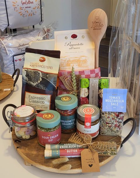 Rundes Servierbrett aus Holz mit vielen Gläsern und Tüten voller Delikatessen darin.