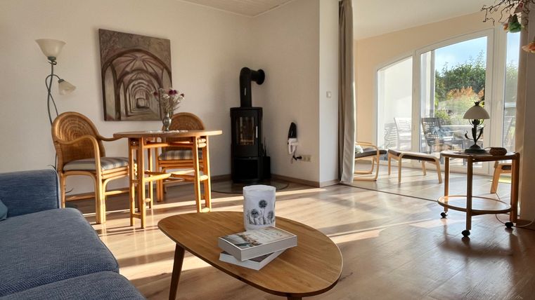 Un salon lumineux et accueillant avec un canapé bleu et une table en bois. De grandes fenêtres laissent entrer beaucoup de lumière naturelle et offrent une vue sur l'extérieur.