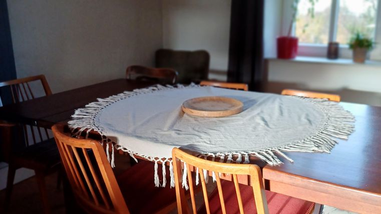Een uitnodigende eetruimte met een houten tafel en stoelen. Een heldere lamp hangt boven de tafel, en de ruimte heeft grote ramen met planten.