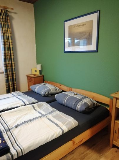 Een gezellige slaapkamer met een tweepersoonsbed en gestreepte kussens. De muren zijn groen en een ingelijst schilderij hangt boven.