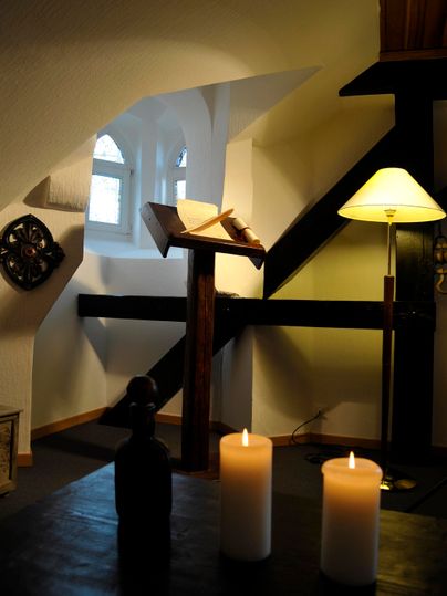 Une pièce confortable avec une lampe et un livre ouvert sur un trépied en bois. Sur la table se trouvent deux bougies allumées.