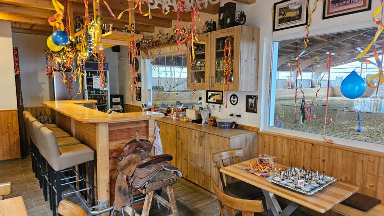Une pièce confortable avec un bar et un intérieur en bois, décorée de rubans colorés et de ballons. Il y a des tables avec des chaises et un jeu d'échecs sur l'une des tables.
