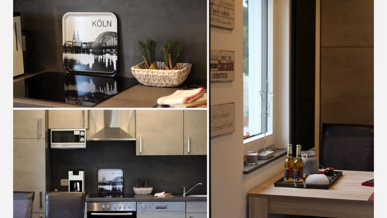 Eine moderne Küche mit Holzschränken und eleganten Geräten. Der Tisch ist liebevoll gedeckt und ein Stadtbild von Köln ist an der Wand zu sehen.