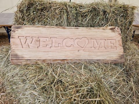 Une plaque en bois avec l'inscription "WELCOME". En arrière-plan, on peut voir de la paille.