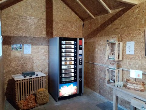 Ein Verkaufsautomat in einem Holzschuppen, umgeben von landwirtschaftlichen Produkten wie Kartoffeln und Eiern in Regalen.