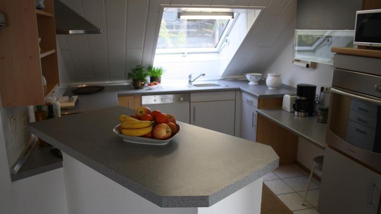 Eine moderne Küche mit hellen Wänden und großen Fenstern. Auf der Arbeitsfläche liegt eine Schale mit Obst.