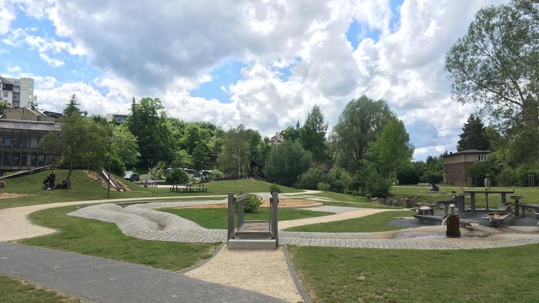Ein schöner Park mit üppigem Grün und geschwungenen Wegen. Die Wolken am Himmel sorgen für eine entspannte Atmosphäre.