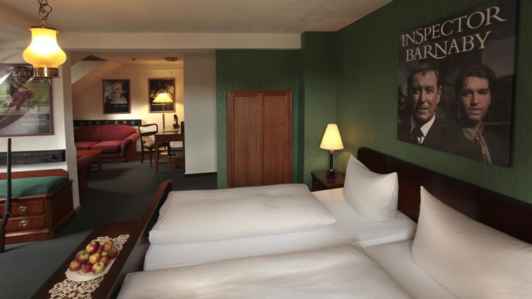 Une chambre d'hôtel confortable avec deux lits et une présentation de pommes sur la table. Un poster de "Inspector Barnaby" est accroché au mur.