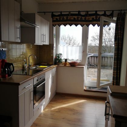 Een lichte keuken met moderne meubels en grote ramen. Het uitzicht naar buiten toont een tuin en een rustige omgeving.