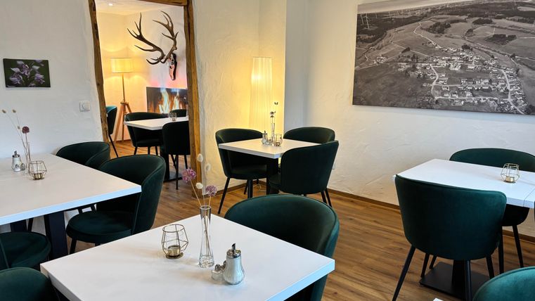 Ein stilvolles Restaurant mit modernen Tischen und grünen Stühlen. An den Wänden hängen Dekorationen, und es gibt sanfte Beleuchtung.