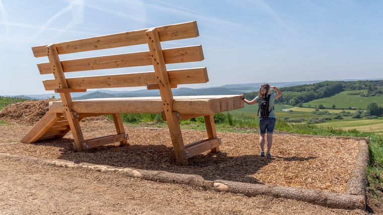 Oversized rustbank met wandelaarster voor uitgestrekt landschap.