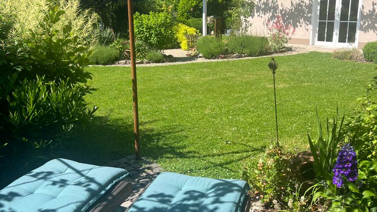 Jardin accueillant avec des chaises longues et une végétation luxuriante. En arrière-plan, une maison moderne est visible.