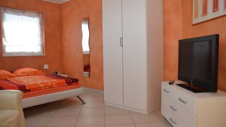 Een gezellige slaapkamer met oranje muren. Er is een bed, een televisie en een kast.