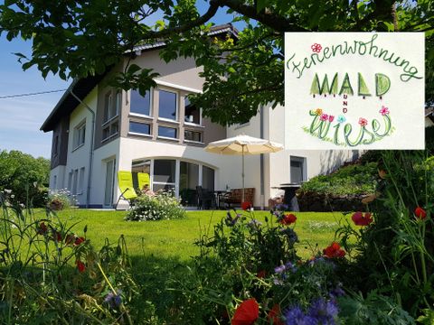 Eine moderne Ferienwohnung mit einem großzügigen Garten und sonnigem Außenbereich. Bunte Blumen und eine Terrasse mit Sonnenschirm laden zum Entspannen ein.
