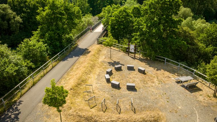 Vogelperspektive auf einen Rastplatz mit Sitzgruppen und einem Weg, umgeben von Bäumen und Grünflächen.