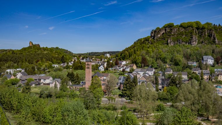 Blcik auf eine Stadt mit vielen Gebäuden und einer großen Kirche im Mittelpunkt. Gebädue umgeben von Bäumen und großen Felsen im Hintergrund.