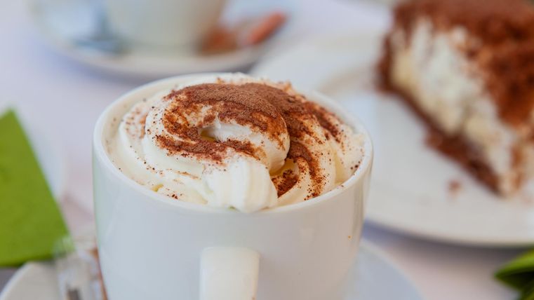 Tasse Kakao und im Hintergrund ein Stück Kuchen