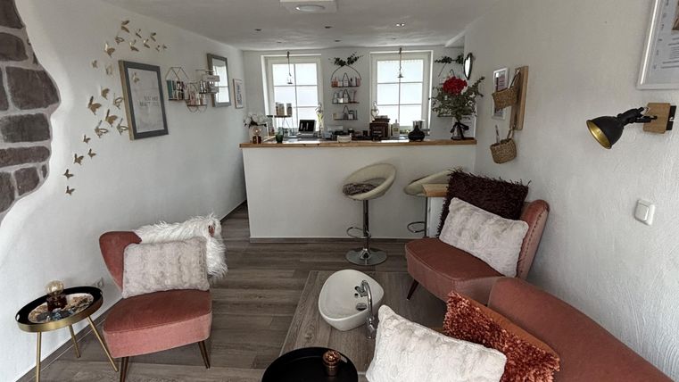 Une salle d'accueil et de bien-être moderne avec des meubles roses et des accents élégants. Il y a une table ronde et des éléments décoratifs sur les murs.