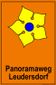 Schild mit gelbem Blütenmotiv und Text 'Panoramaweg Leudersdorf' auf orangefarbenem Hintergrund.