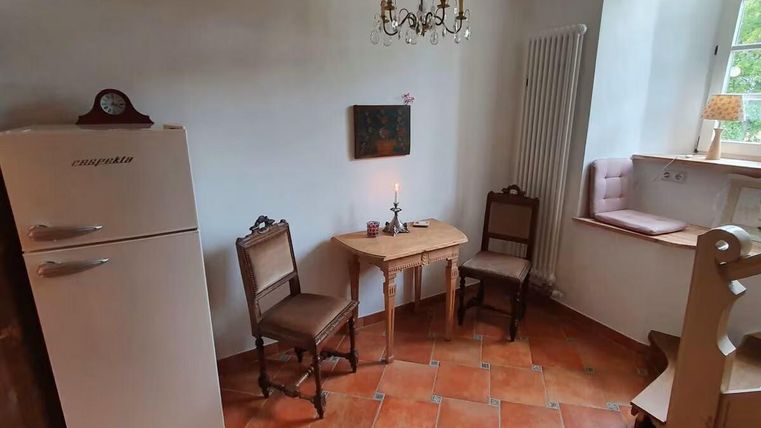 Ein kleiner Raum mit einem Kühlschrank, einem Tisch und zwei Stühlen. Die Wände sind hell und es gibt eine gemütliche Fensternische.