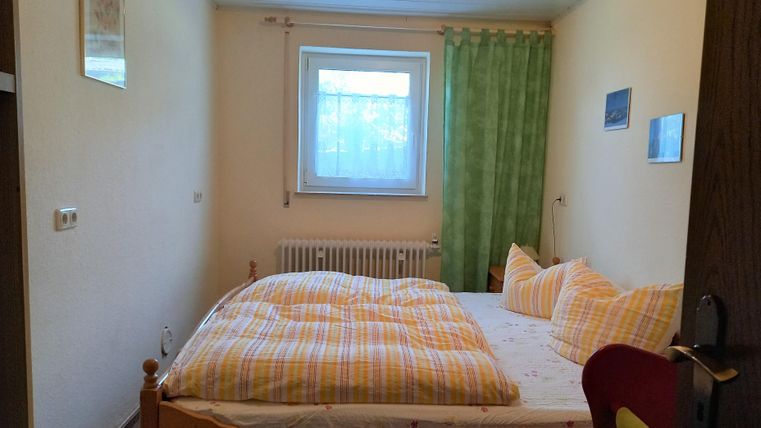 A cozy bedroom with a double bed and yellow-striped bedcovers. A window with green curtains provides light and a friendly impression.