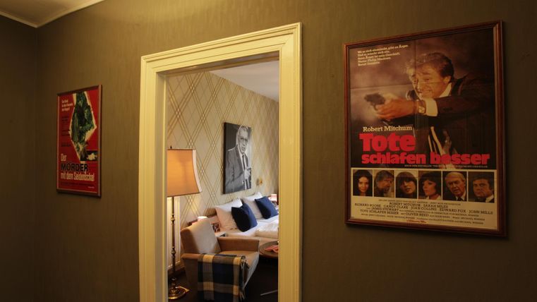 Un couloir confortable avec des affiches de films sur les murs. Par la porte, une pièce accueillante avec un lit et des coussins décoratifs est visible.