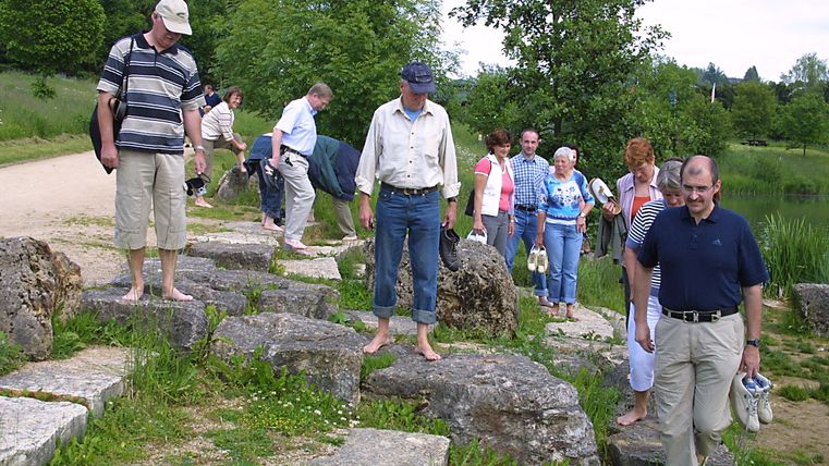 Gruppe von Menschen geht barfuß über Steine in einem Park.