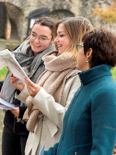 Drei Frauen im Freien, die gemeinsam ein Dokument betrachten und lächeln.