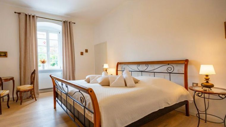 Ein helles Schlafzimmer mit einem großen Doppelbett und dekorativen Kissen. Die Fenster lassen viel Tageslicht herein und die Einrichtung ist warm und einladend.