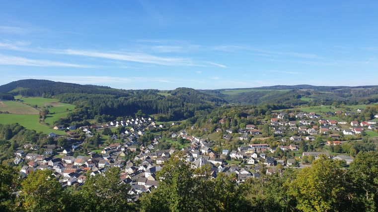Een schilderachtig dorp in een groene landschap onder een heldere blauwe lucht. De zachte heuvels omringen de huizen en creëren een rustige sfeer.