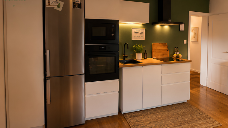 A modern kitchen with white cabinets and a wood countertop. It is well-lit and has an elegant look.