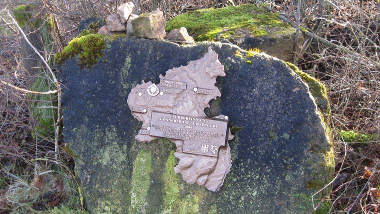 Ein Gedenkstein mit einer Karte und Inschrift, umgeben von Moos und Gras.