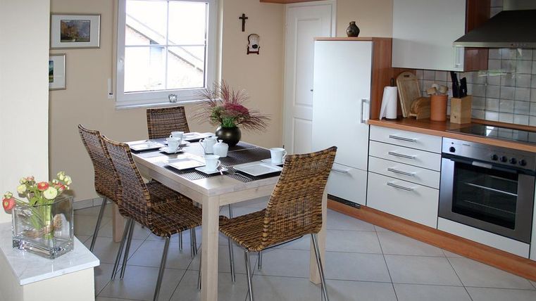 Een lichte en moderne keuken met een eettafel en vier stoelen. Op de tafel liggen servies en een bloemenvaas.